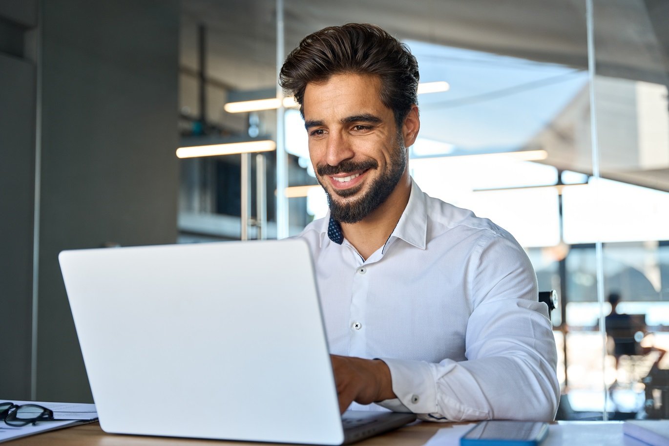 Happy young Latin business man looking at laptop at work. Smiling businessman professional employee, company manager using computer sitting at desk managing digital data in office.; Shutterstock ID 2339480247; purchase_order:09940; job:Job Optimism MC24-0172; client:Robert Half; other:Marissa Hoffman for Alison Hoa and Millie Lee
